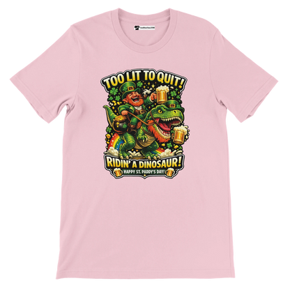 Pink St. Patrick's Day tee with leprechaun riding dinosaur, holding beer, 'Too Lit to Quit' text, shamrocks, rainbow