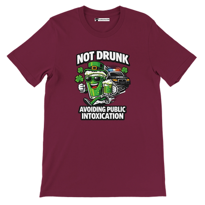 Maroon tee with cartoon beer mug, police car, clovers, and text 'Not Drunk Avoiding Public Intoxication'.